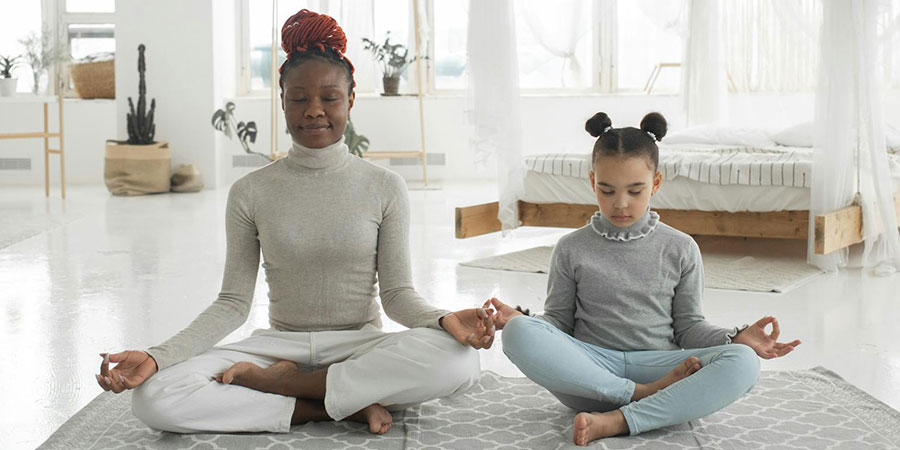a black woman with a kid beside her practicing yoga in Lotus pose